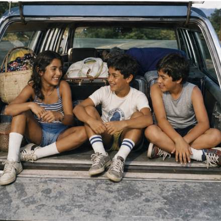 Three children sitting in the open tailgate of a station wagon